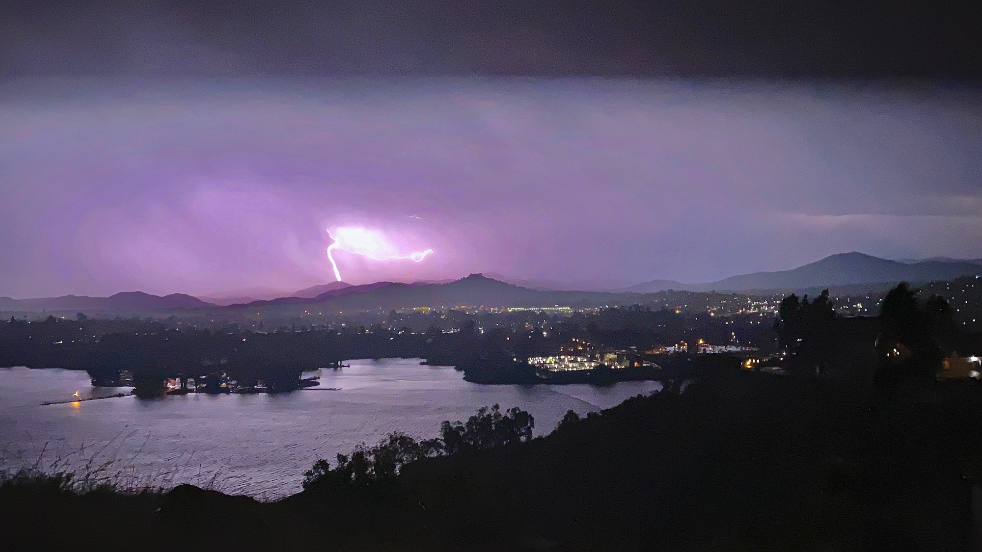 A bolt of lightning strikes a mountain and lights up the sky purple, over Lake Murray